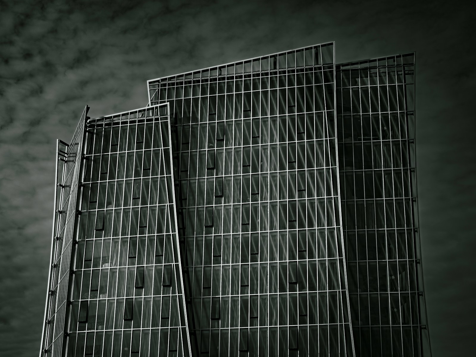 Modern skyscraper with geometric facade against cloudy sky